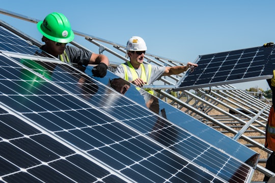 Workers wearing hardhats install solar panels at a solar field