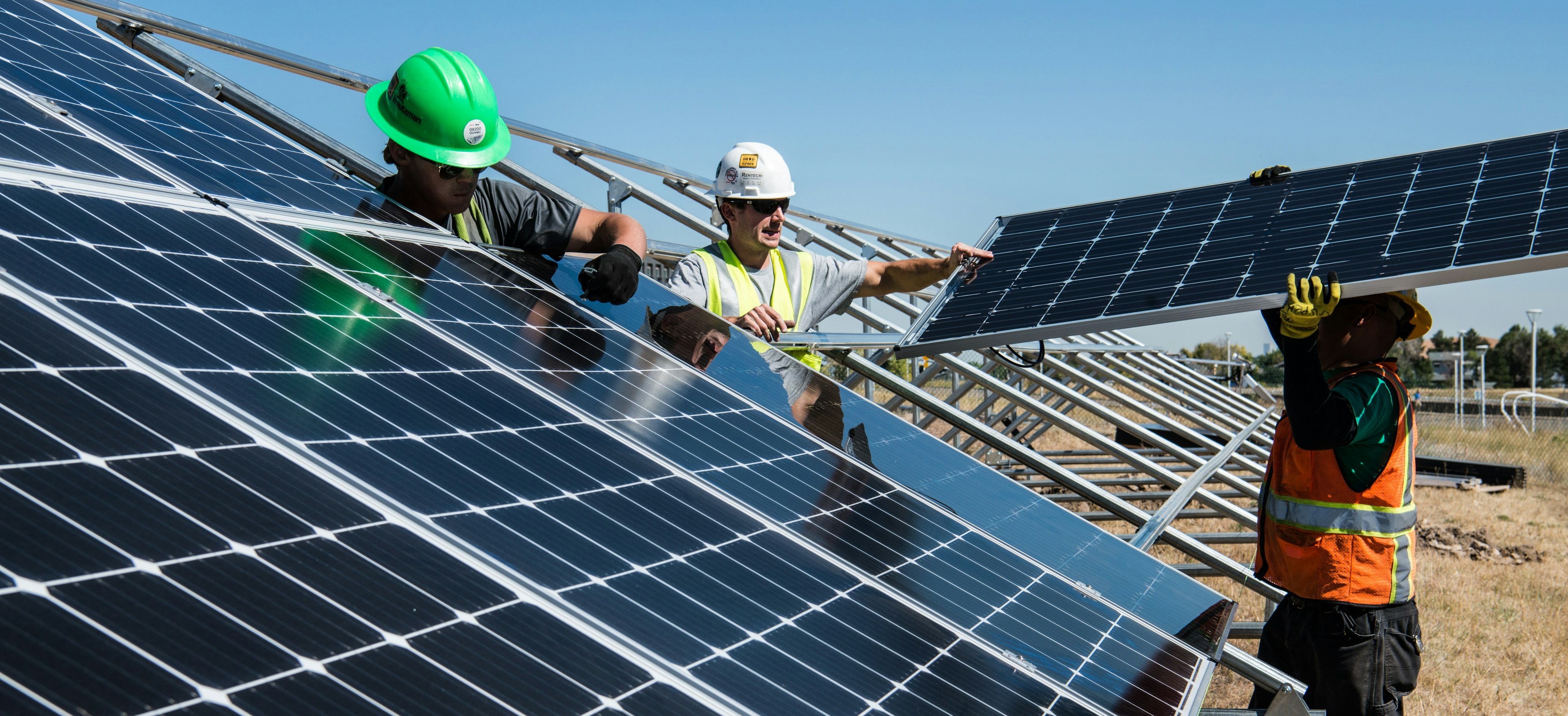 Workers wearing hardhats install solar panels at a solar field