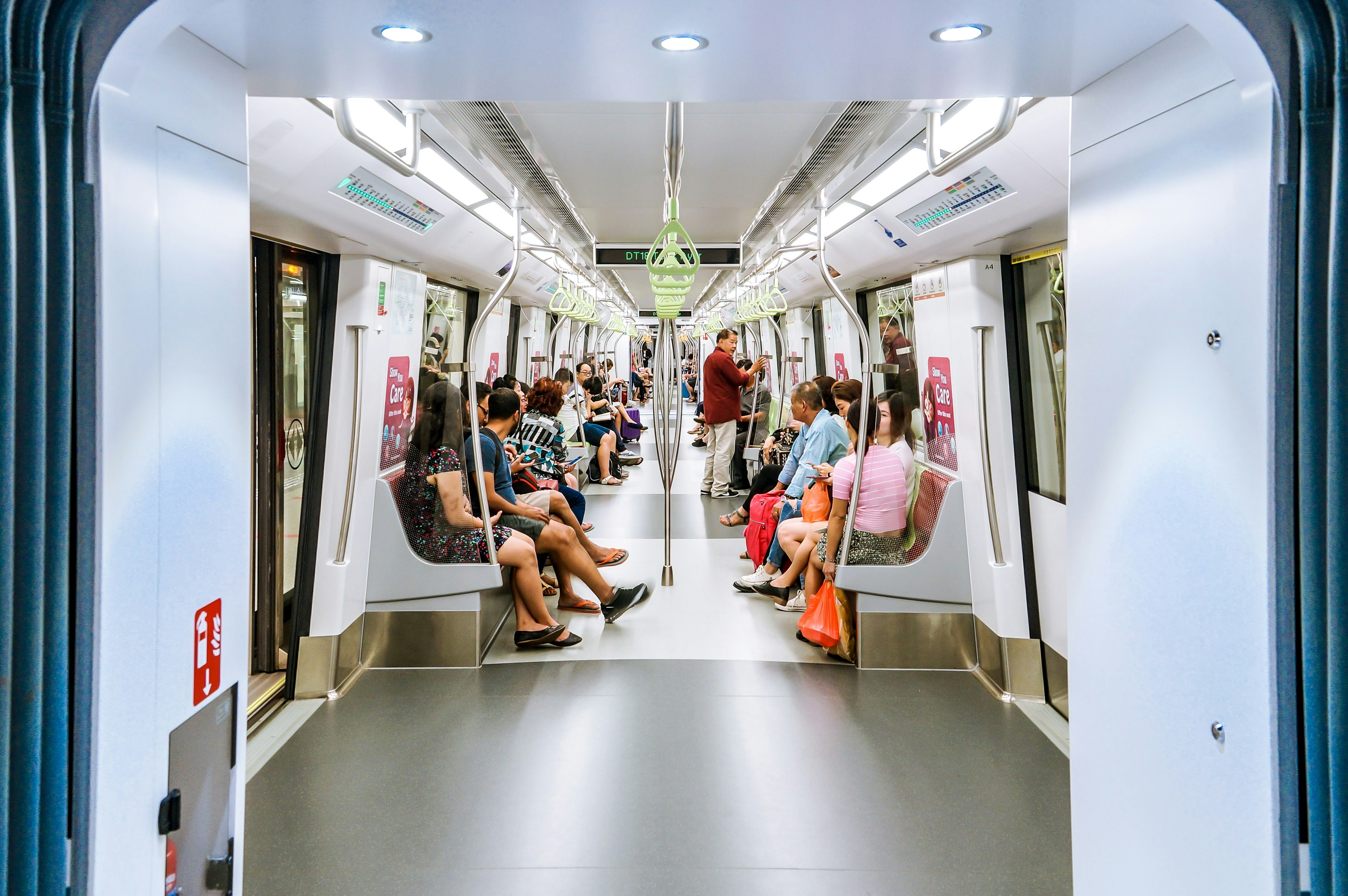 a photo from inside singapore's subway system, with people sitting on benches in a clean white car
