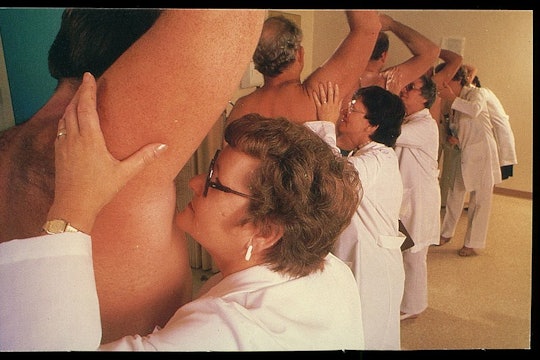 a line of women wearing lab coats smelling the armpits of a bunch of men