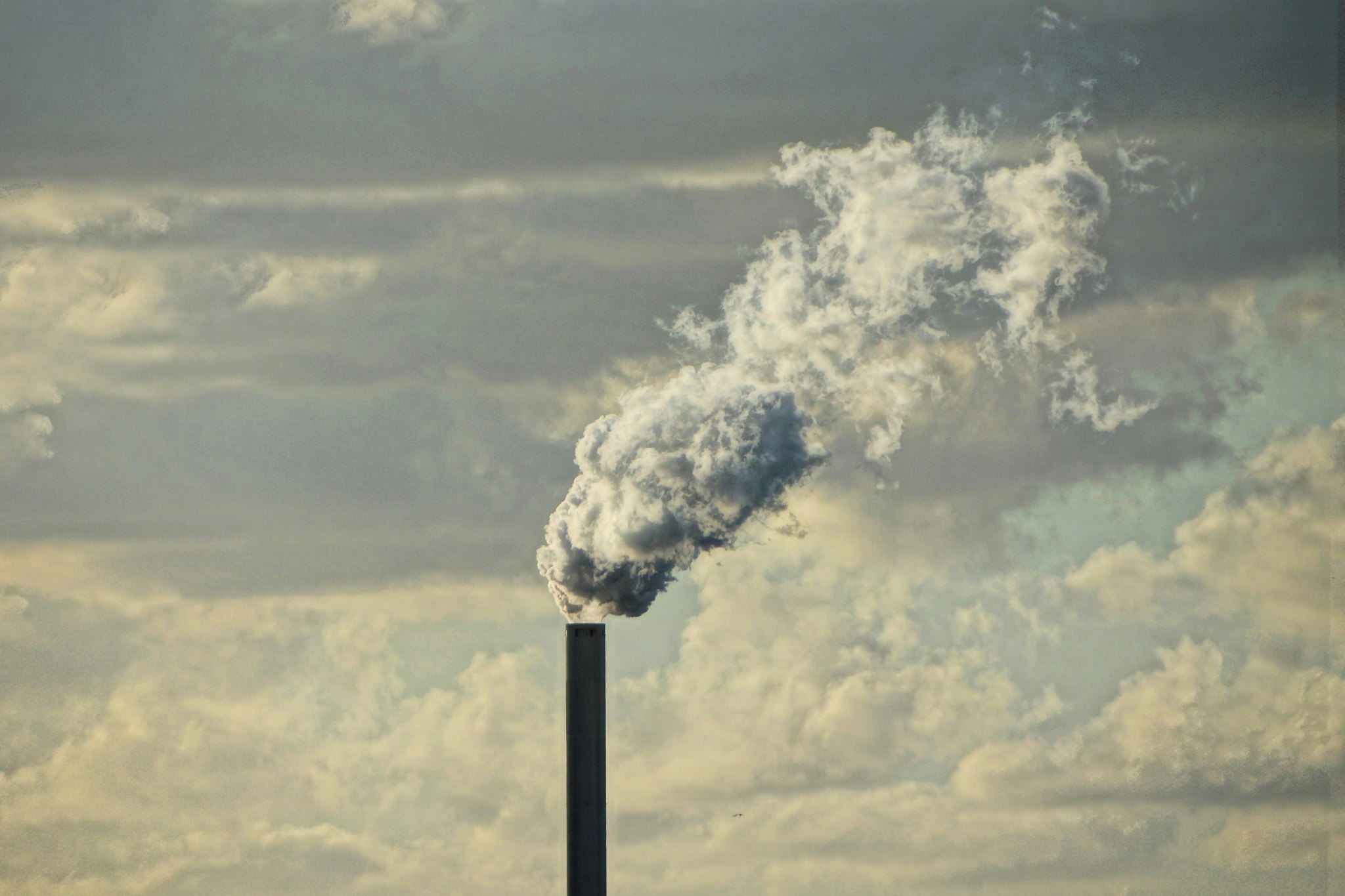 White smoke emerging from a smokestack, against a backdrop of clouds.