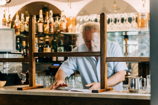 A bartender collects money from behind a plastic shield erected to protect him from COVID-19