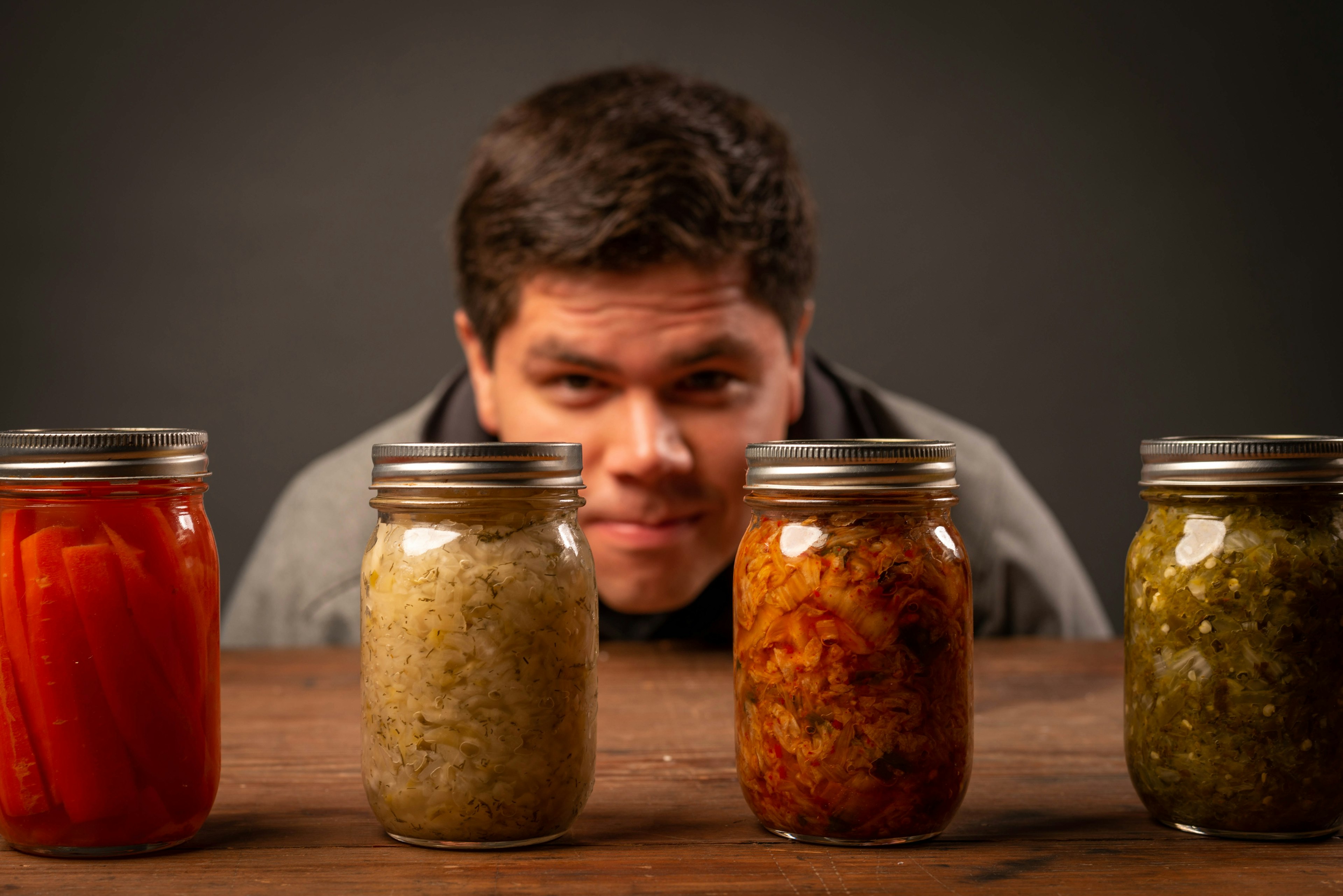 man sitting behind 4 jars of fermented foods