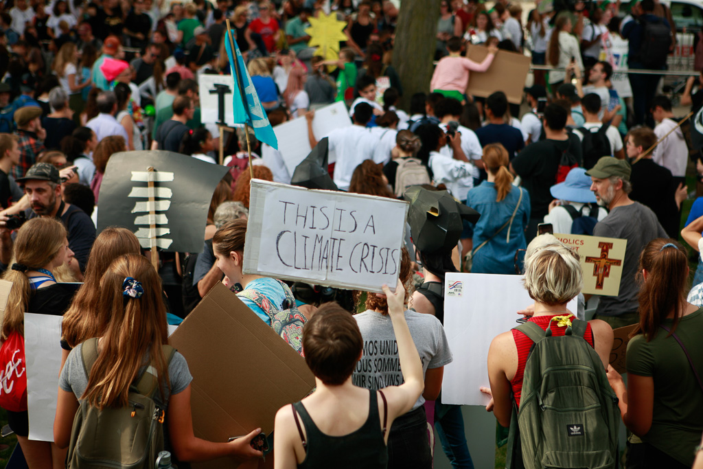 A shot of the backs of a crowd of climate strikers in Chicago, IL, USA. One is holding a sign that reads "This is a climate crisis."