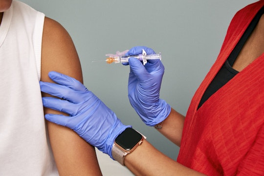 A close-up of a syringe and needle carrying a vaccine, about to be injected into a patient's arm