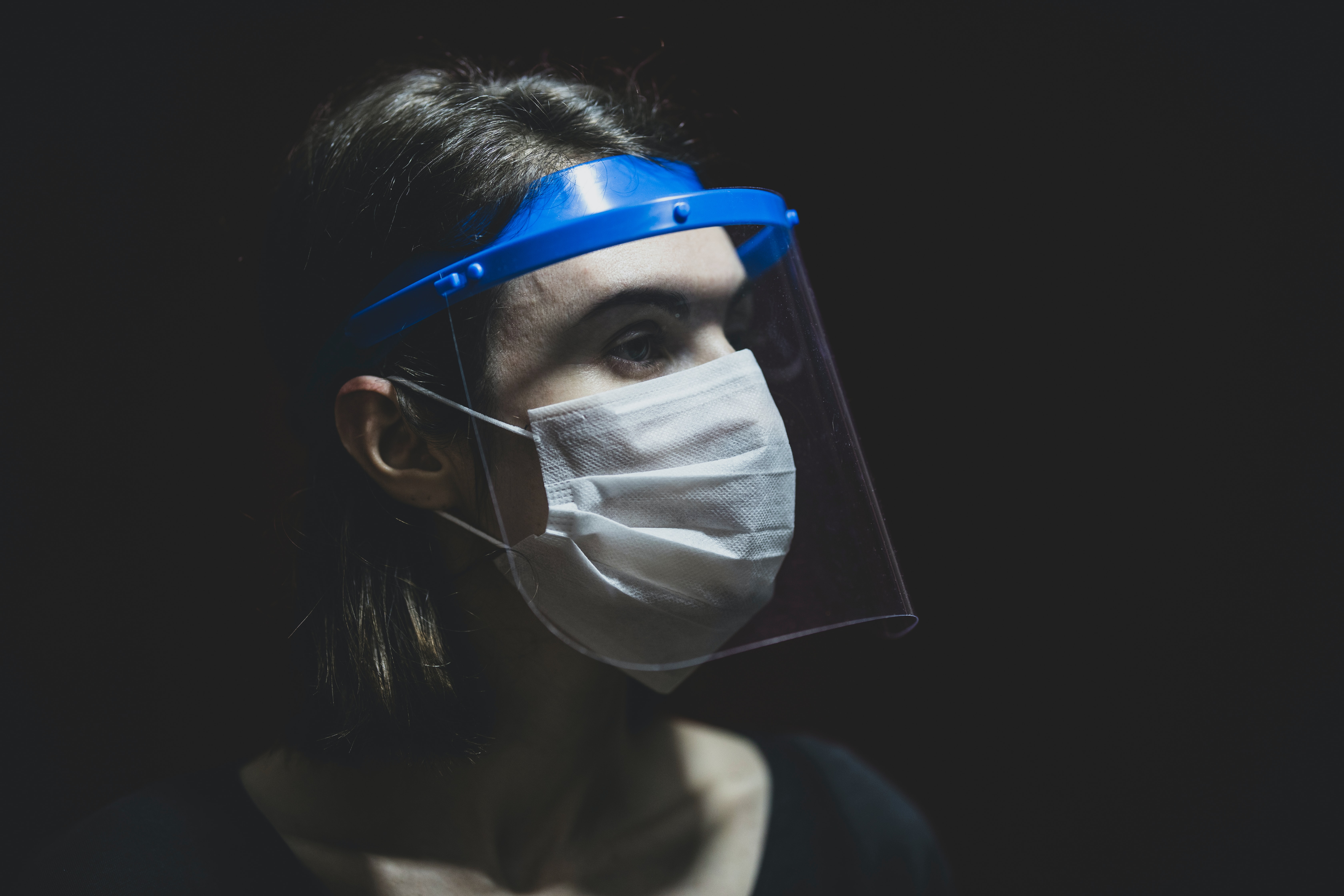 a woman wearing a mask and face shield against a dark background