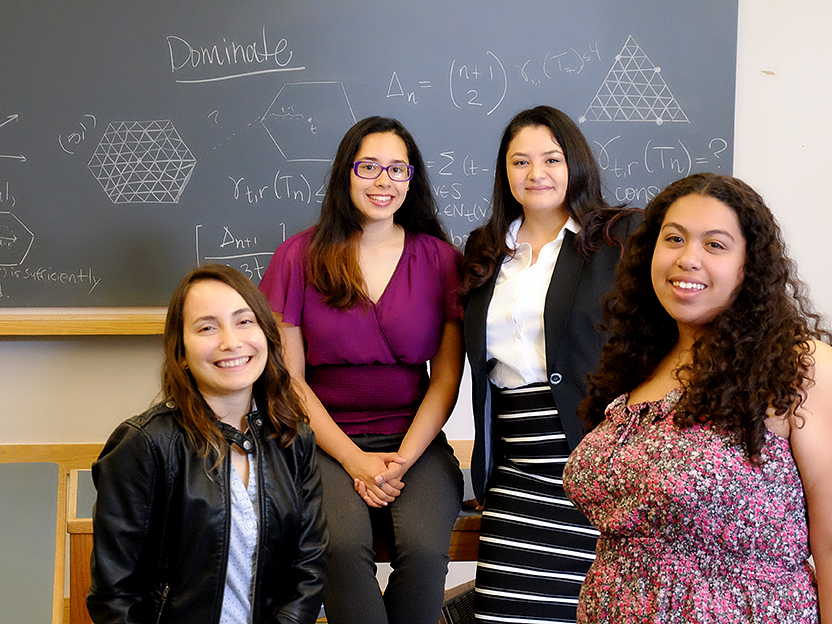 pamela harris and three students smile in front of a math-filled chalkboard