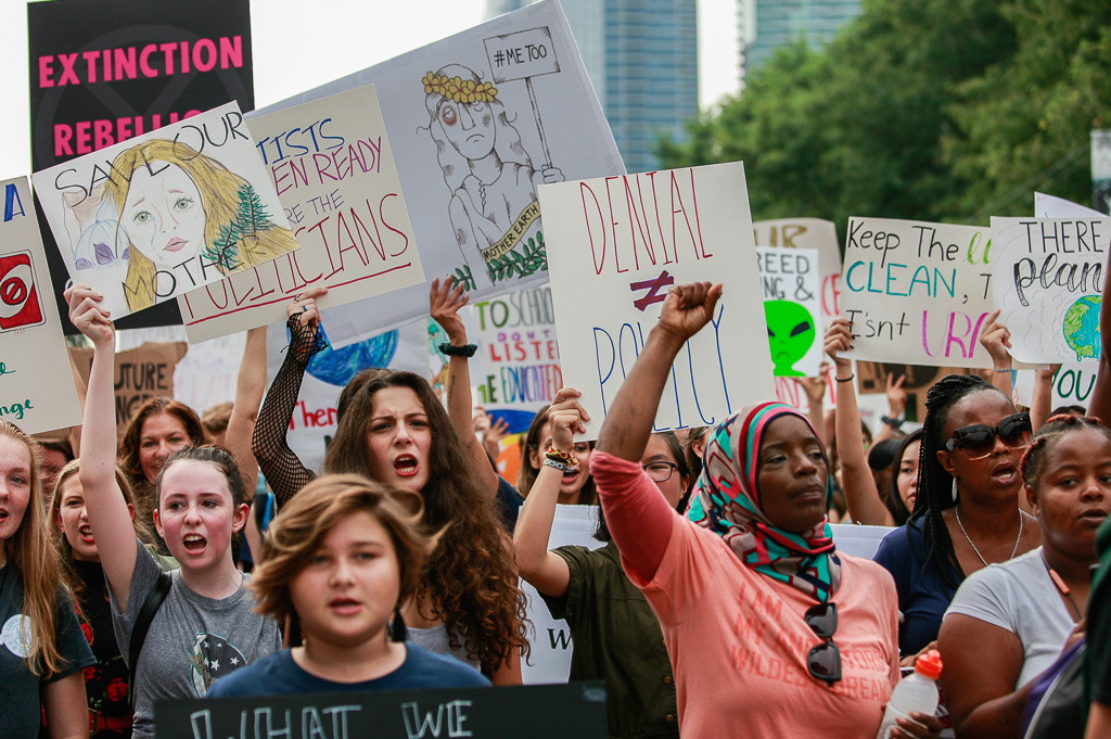 A crowd of climate strikers in Chicago, IL, USA, marching down the street holding signs and their fists in the air.