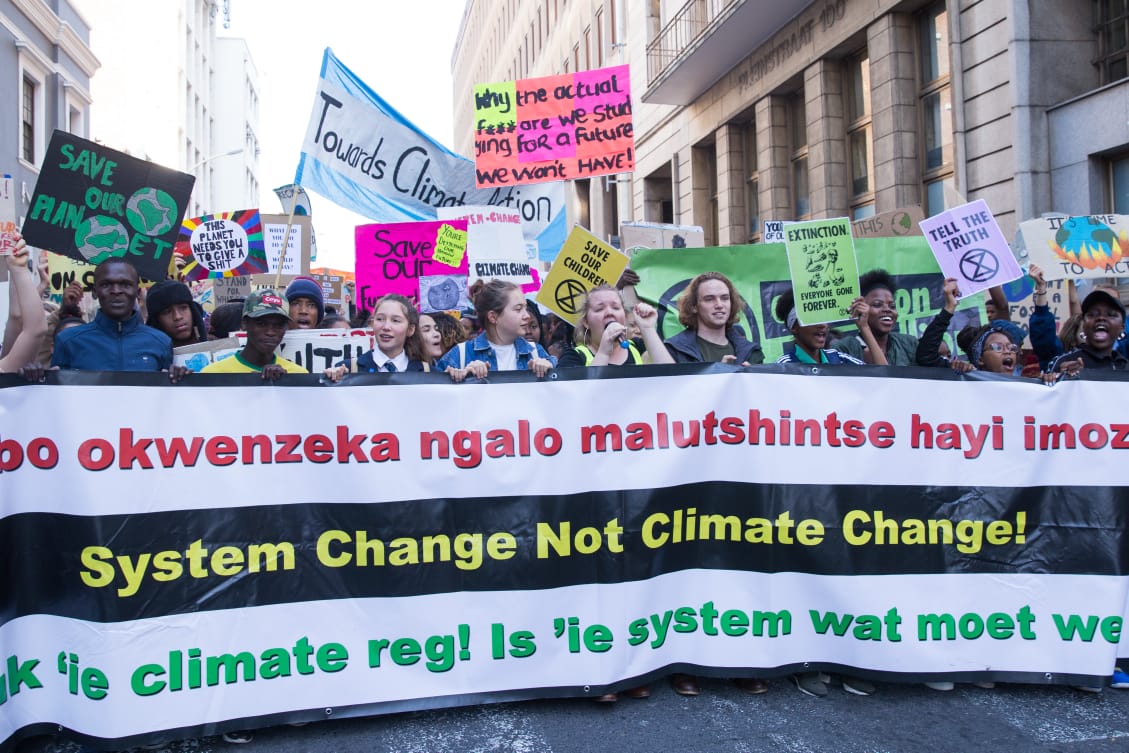 Climate strikes in South Africa holding a large sign that reads "System Change Not Climate Change!"