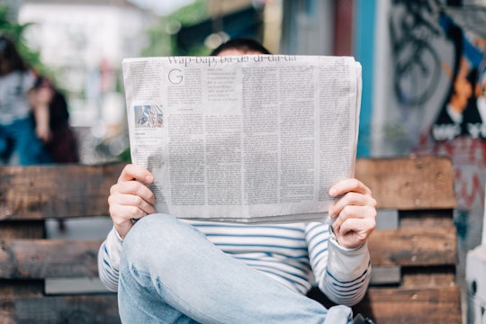 A man sitting on a bench reading a newspaper.