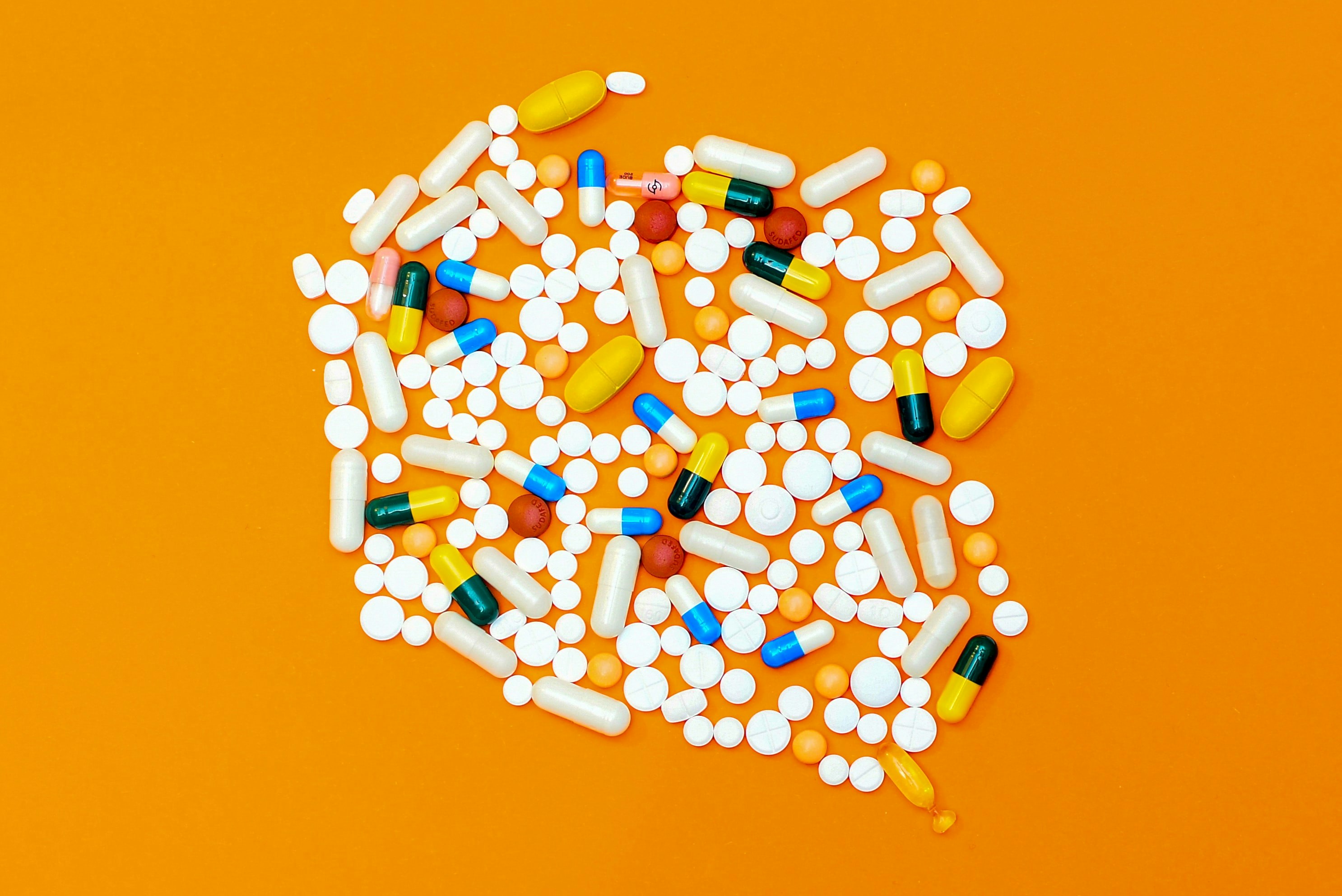 a pile of white and colored pills against a bright orange background