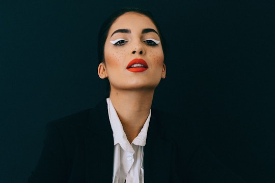 A woman wearing red lipstick, painted on freckles, and white eyeshadow shaped to look like wings.