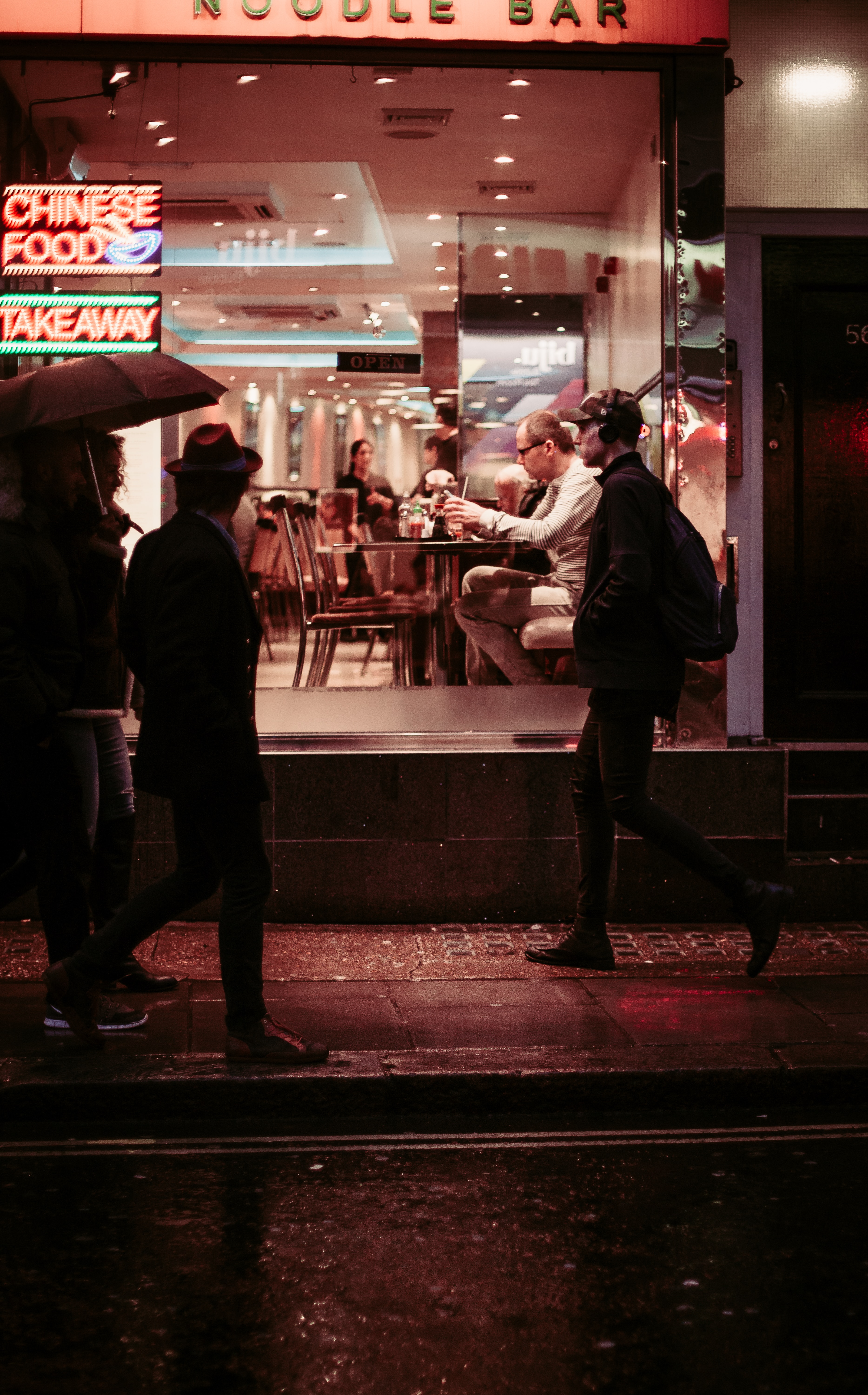 People walking at night past the window of a Chinese restaurant.