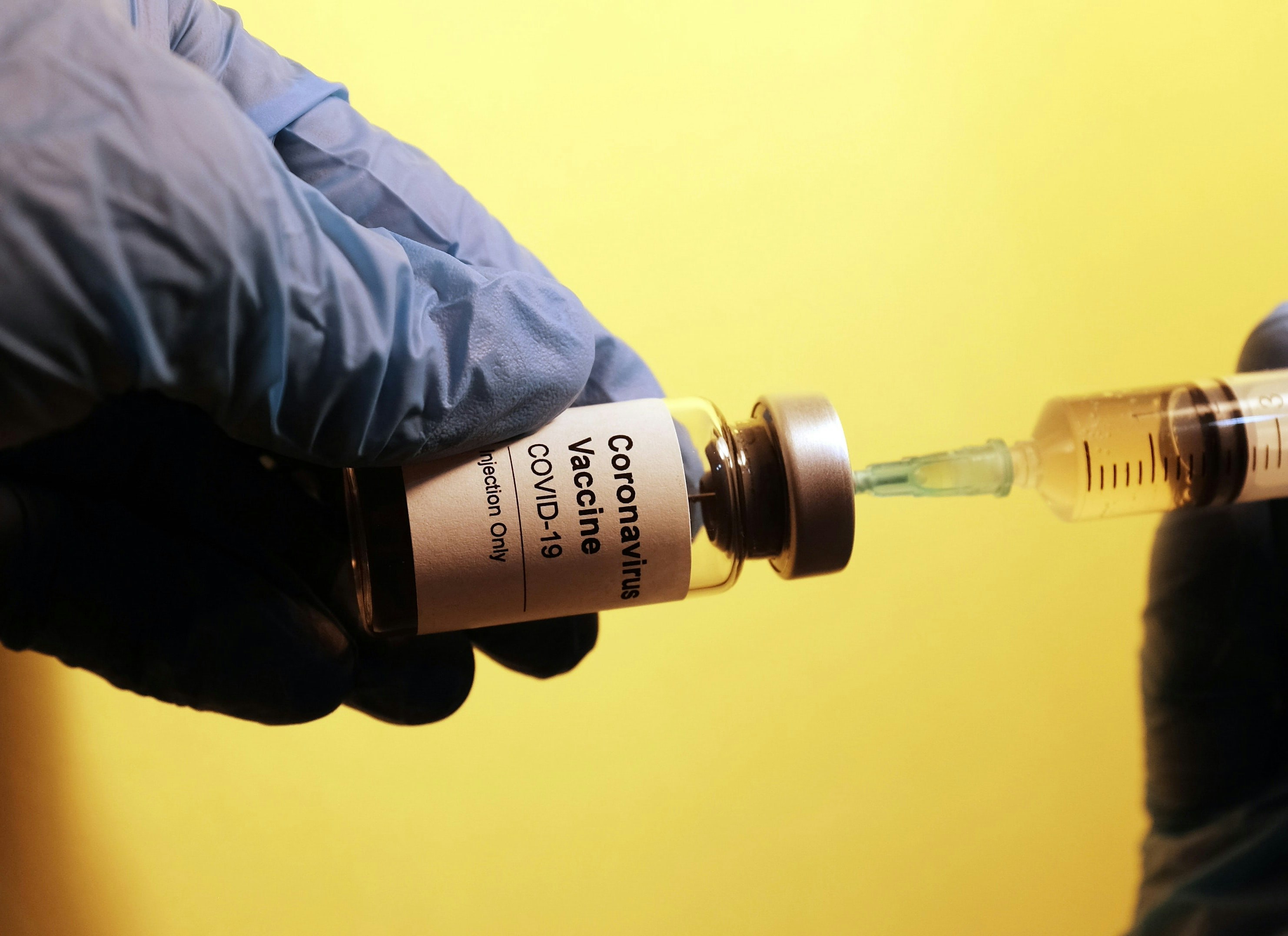 A syringe pulling from a vial labeled "coronavirus vaccine, COVID-19"