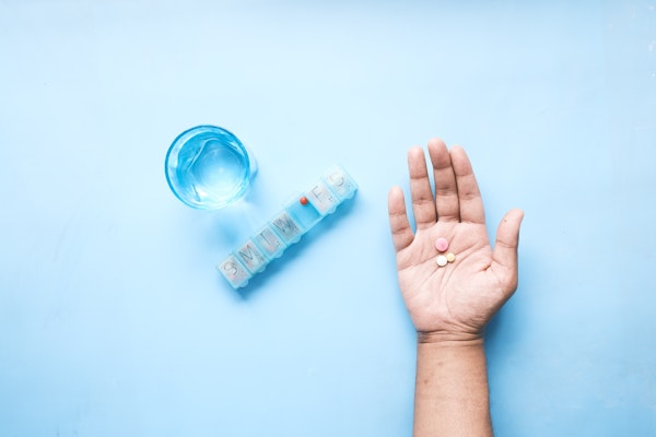 a hand holding some pills next to a pill keeper and a glass of water