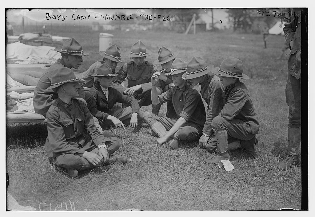 Boys sitting cross-legged on the ground playing "mumble-the-peg" knife game