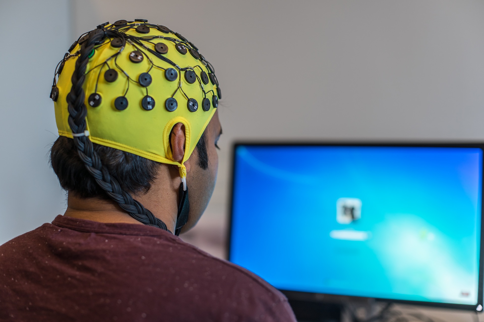 a man wearing a cap covered with eeg electrodes and watching a screen