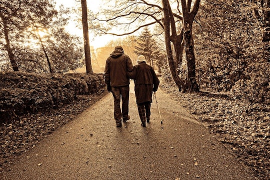 sepia tone photo of two people walking, one is elderly and using a cane