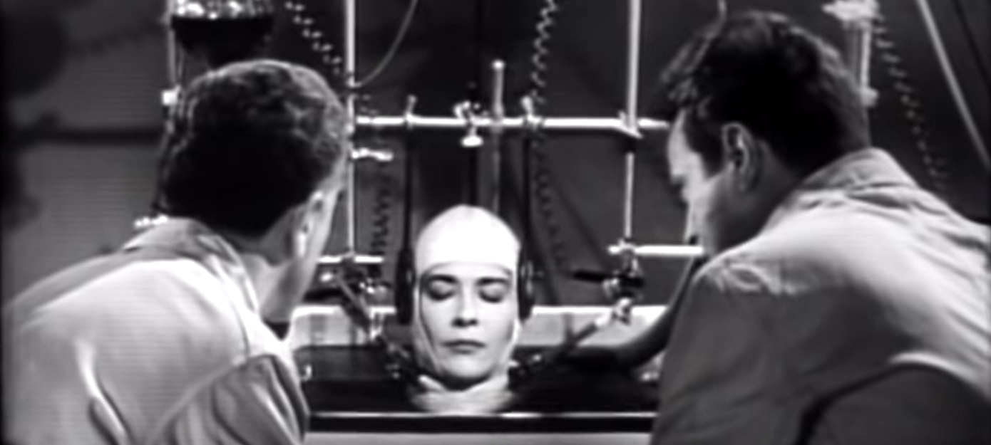 A still from the movie "The Brain That Wouldn't Die", 1962. Two scientists contemplate a woman's head kept alive in a lab.